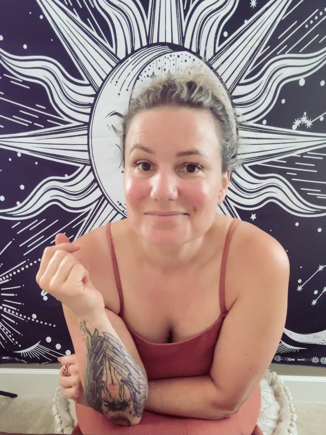 Tracy Brown leaning forward with her arms folded, smiling at the camera in front of a sun and moon tapestry